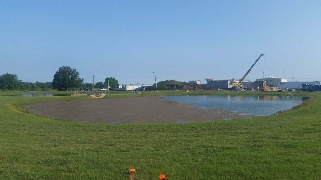 A photo of a water retention pond with visible algae and invasive plants.