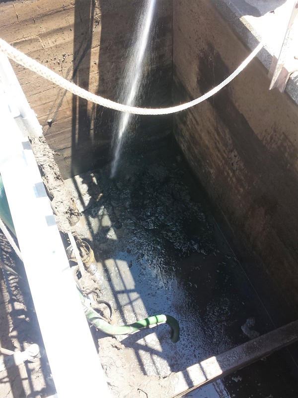A industrial dewatering services being performed in a water tank containing debris and sludge.