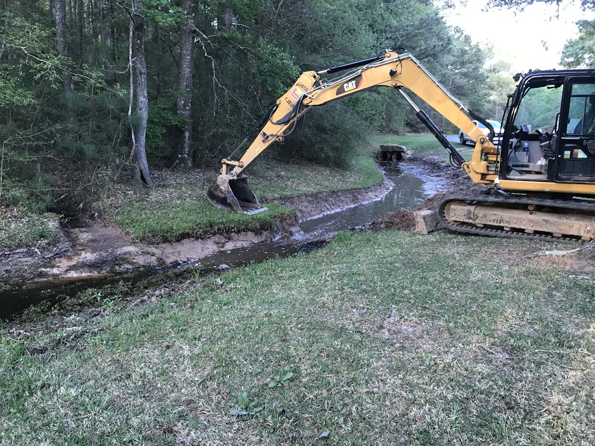 A large excavator performing civil construction services by cutting swale in Texas.