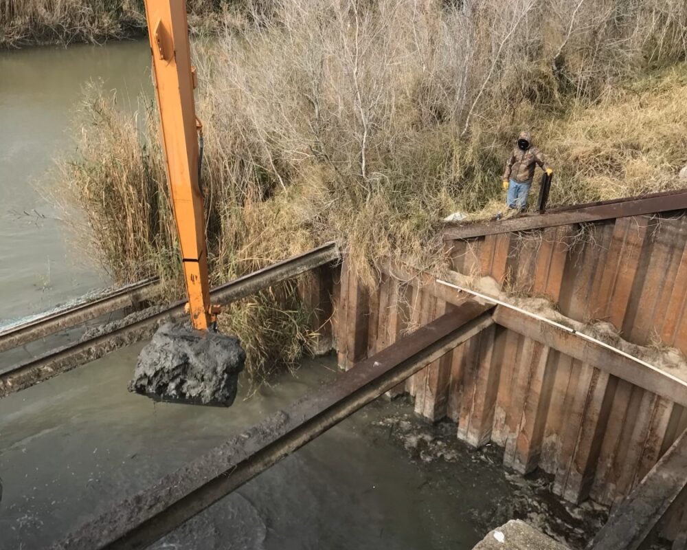 A large excavator demonstrating exceptional reach and precision while tackling excavation work on a steep embankment by a riverside. This scene showcases Bullock Construction's specialized dredging equipment's ability to operate effectively in difficult terrains, proving its capability to access areas traditionally considered hard to reach with ease.