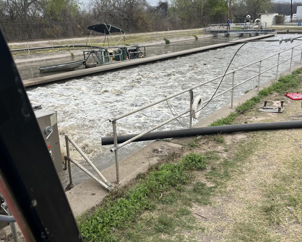 A wastewater treatment facility with a canal undergoing dredging to remove accumulated sludge and debris.