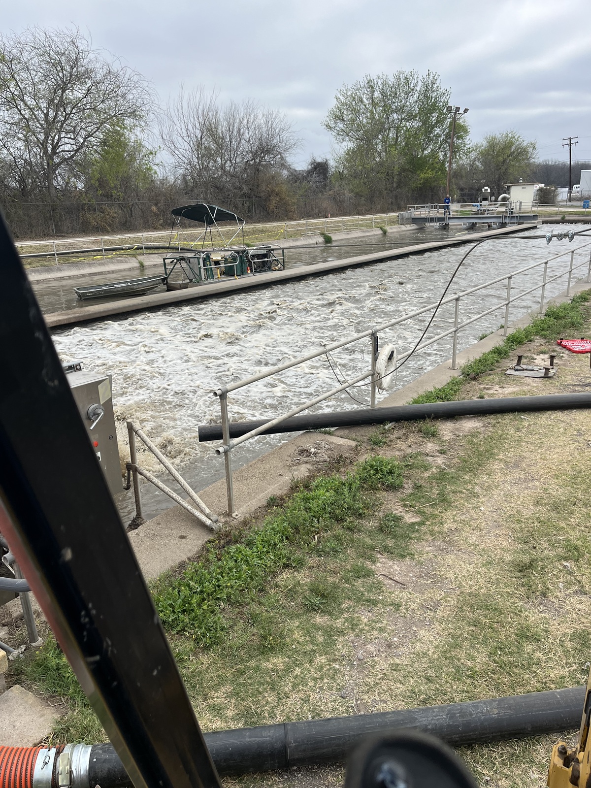A wastewater treatment facility with a canal undergoing dredging to remove accumulated sludge and debris.