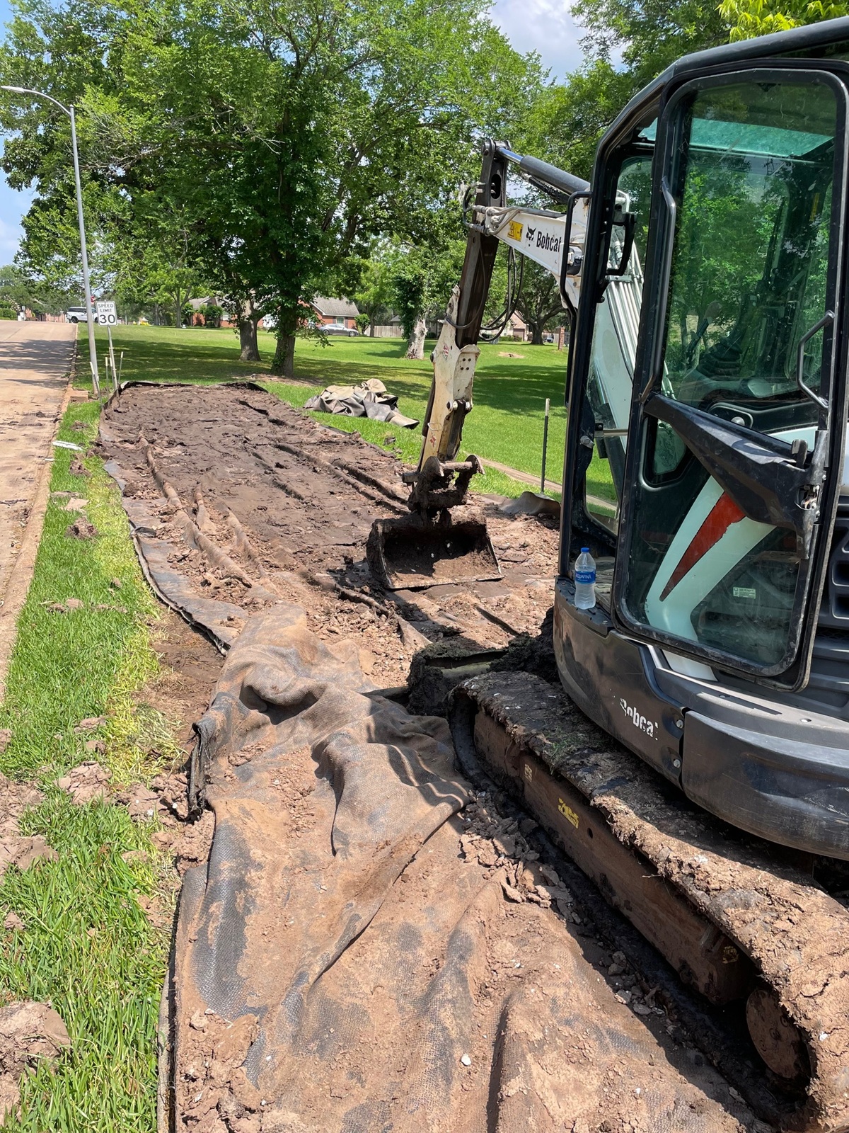Removal of dewatering bag after completion of a water retention pond dredging project. An excavator is rolling along the black lining removing all water and sediment before removal.