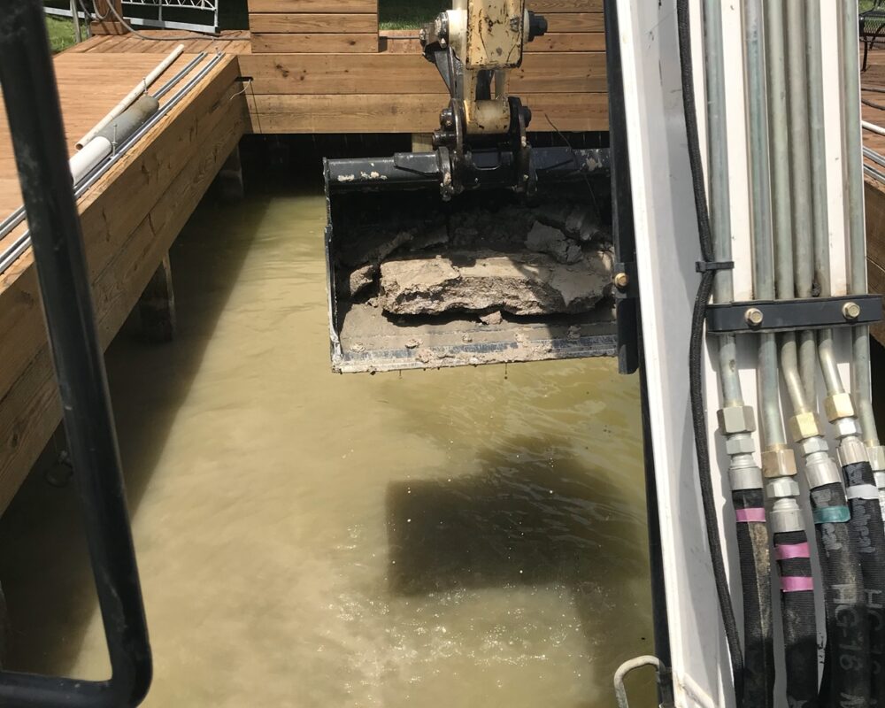 A photo of a excavator working in a boat slip removing accumulated mud and sediment.