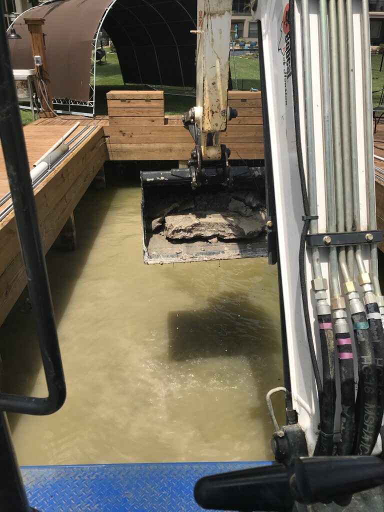 A photo of a excavator working in a boat slip removing accumulated mud and sediment.