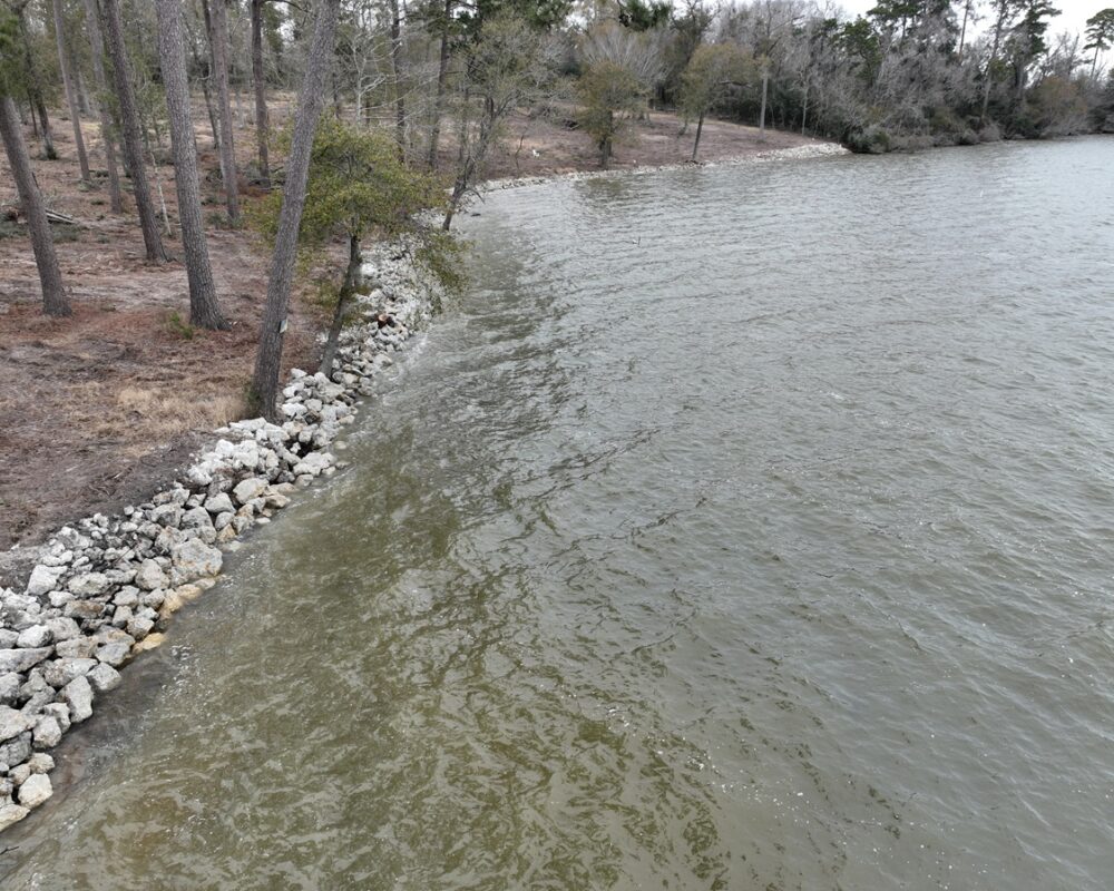 Riprap rocks placed strategically along a lake shoreline as a protective barrier against erosion, surrounded by natural greenery.