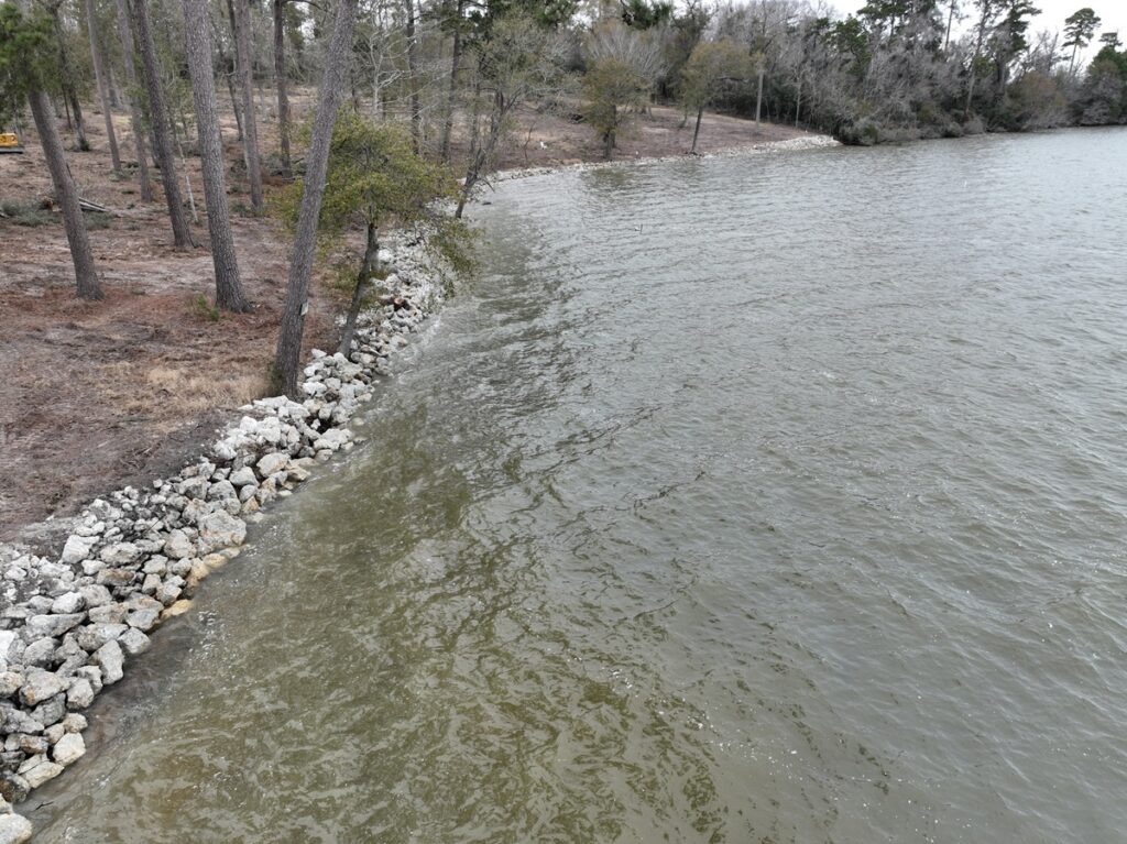 Riprap rocks placed strategically along a lake shoreline as a protective barrier against erosion, surrounded by natural greenery.
