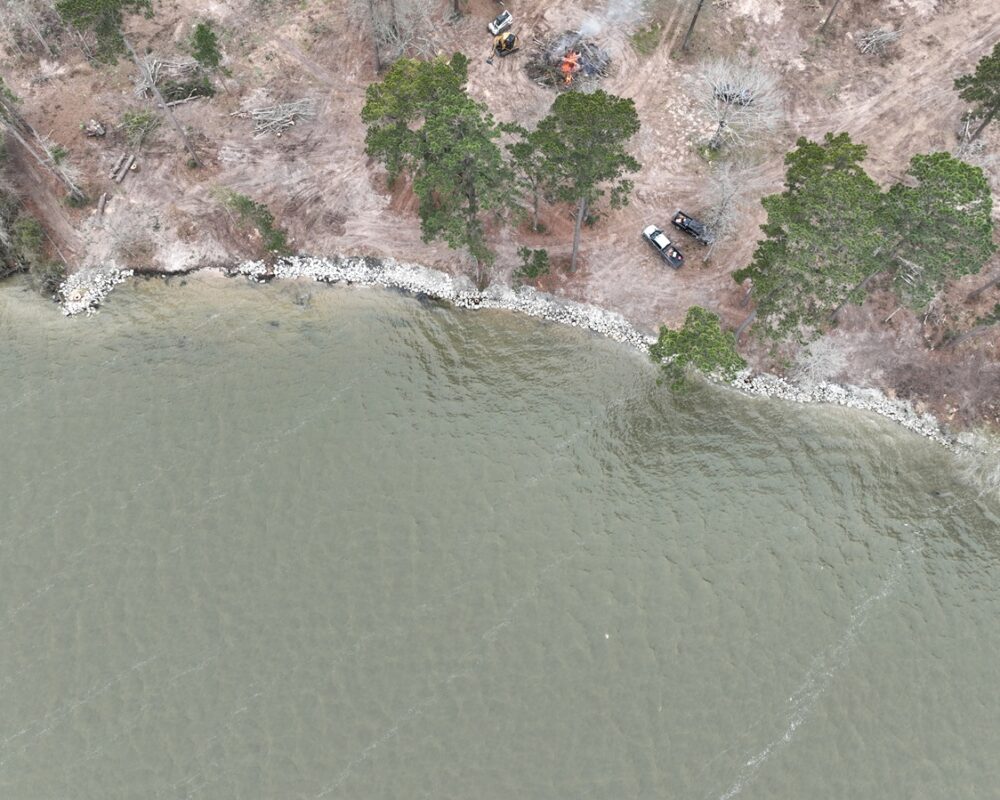 Riprap rocks covering the edge of a lake shoreline, demonstrating erosion prevention within a forested area.