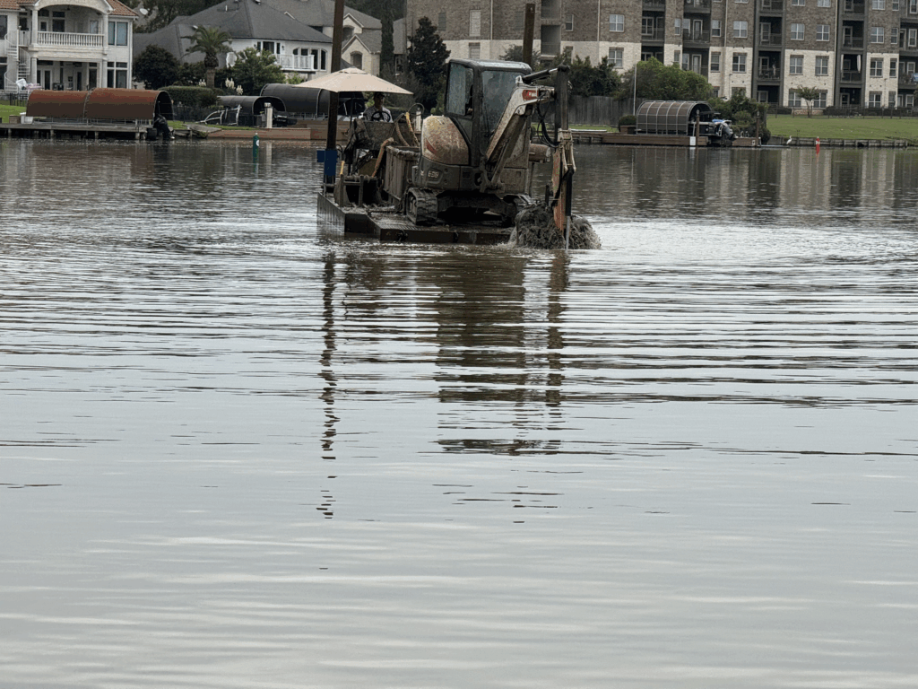 An image of a small, compact barge with a small excavator and mud box removing silt and debris from the bottom of a residential canal.